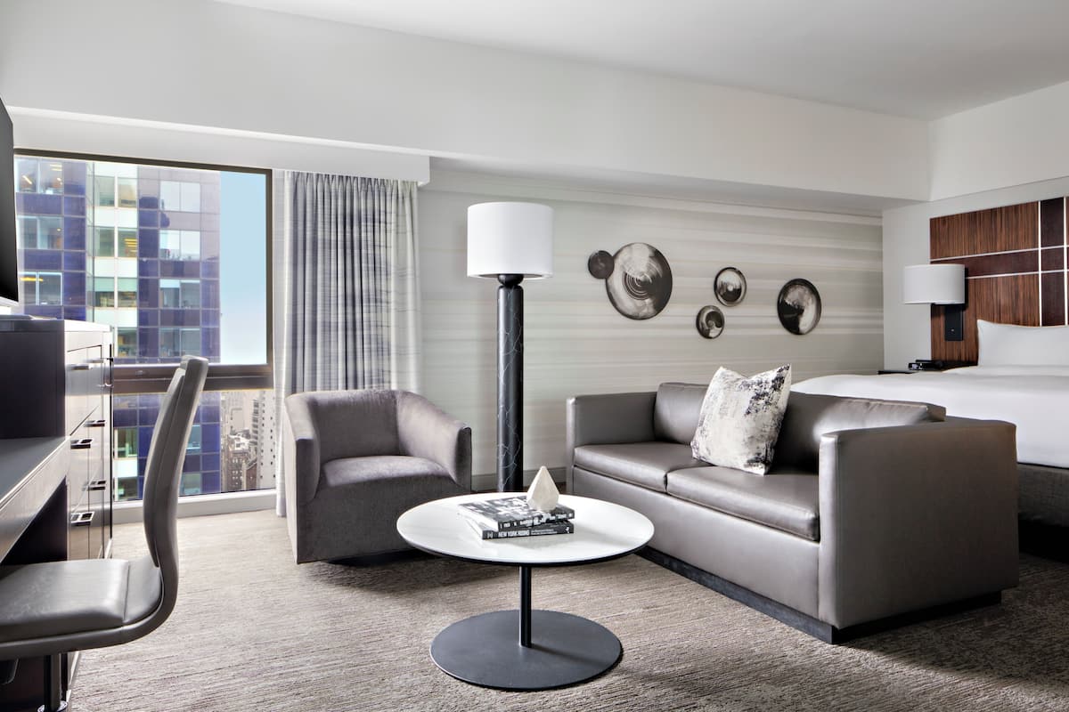 Een moderne hotelkamer met een bank, fauteuil en een kleine ronde tafel met een lamp.