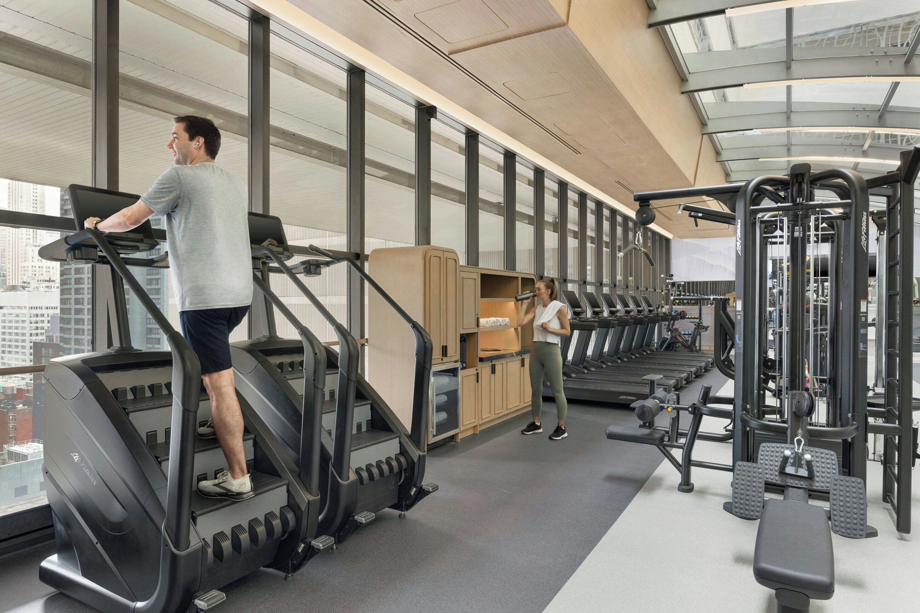 A gym with treadmills, weight machines, and a large window with a city view.