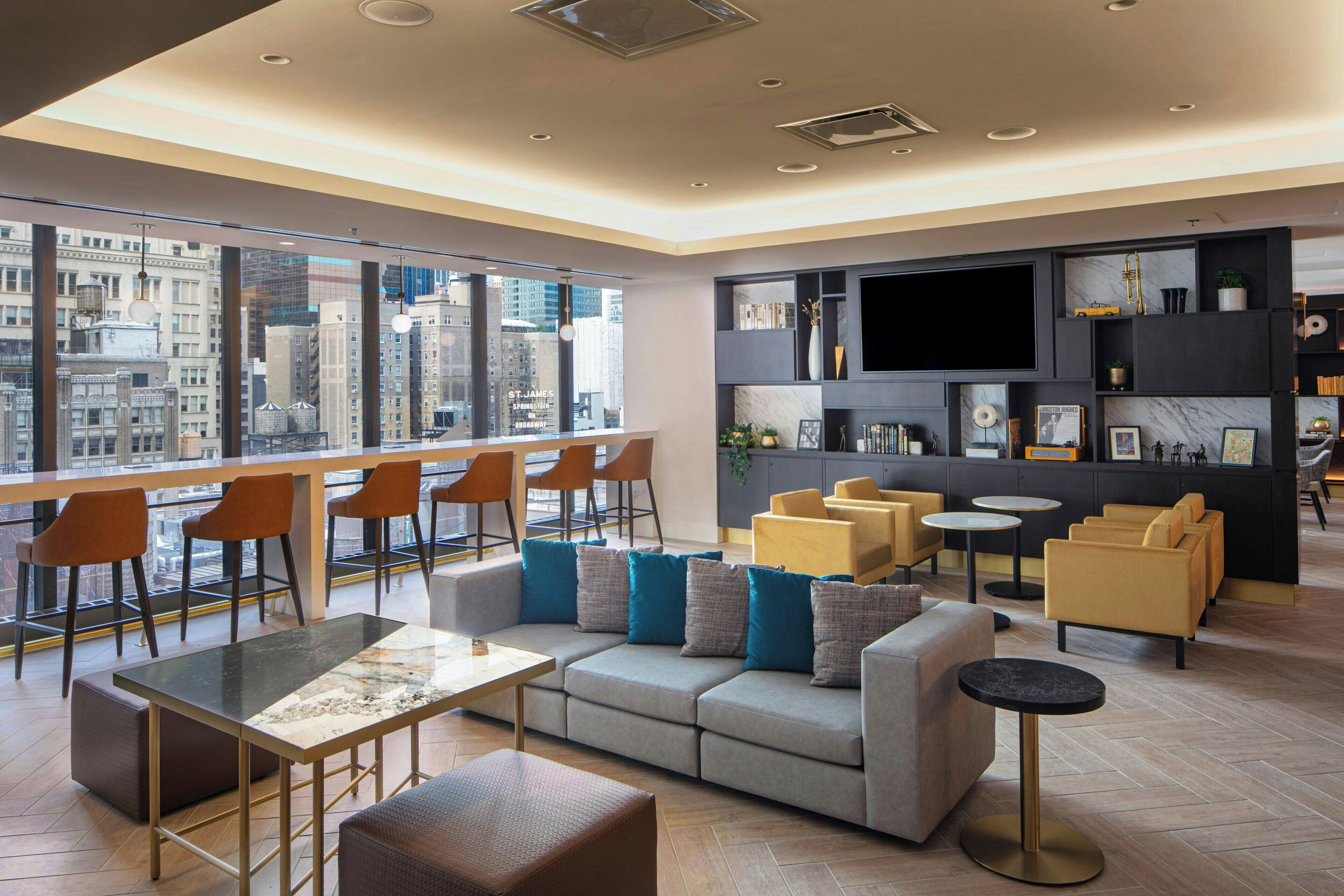 A modern living room with a large window, a sofa set, a dining table, and a bar area.