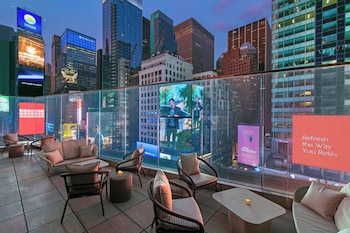 A spacious lounge with a large bar area, seating arrangements, and a view of the cityscape through large windows. at New York Marriott Marquis