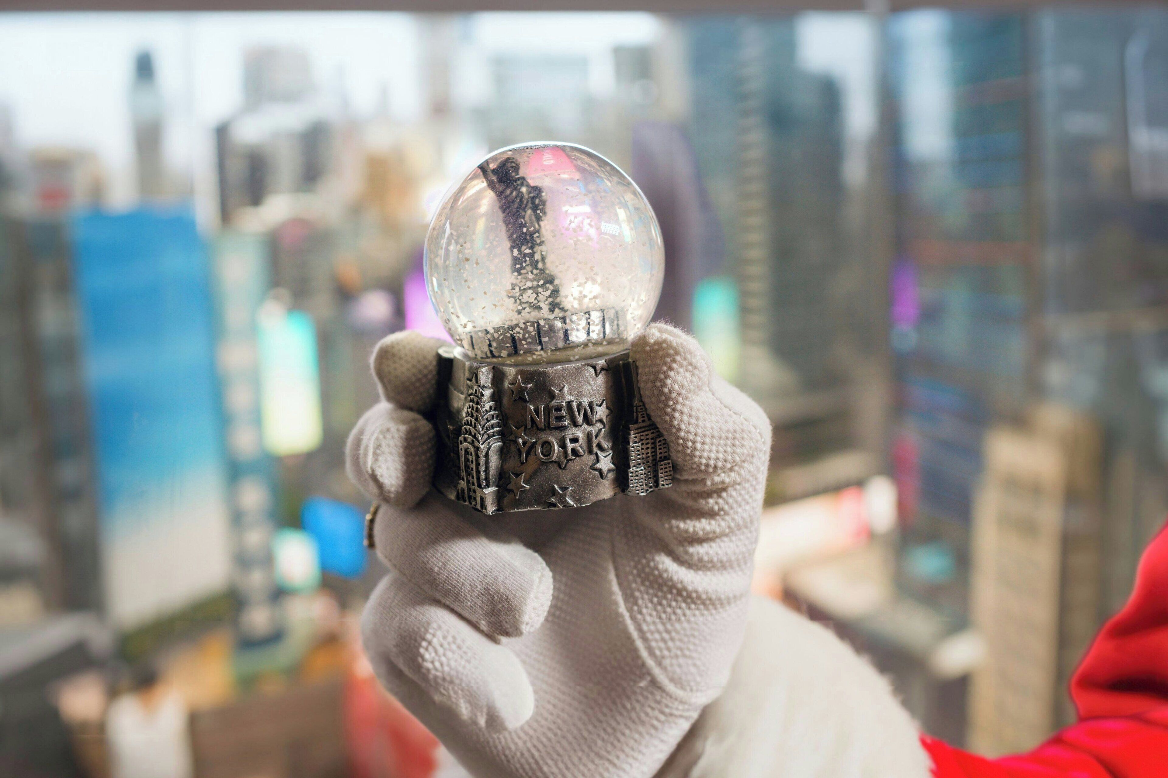 A person holding a snow globe with "NEW YORK" written on it, with a cityscape in the background.