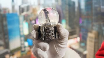 A person holding a snow globe with "NEW YORK" written on it, with a cityscape in the background.