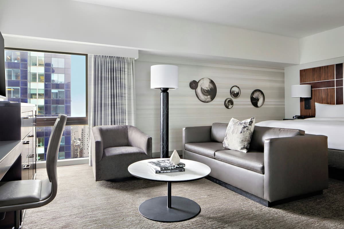 Een moderne hotelkamer met een bank, fauteuil en een kleine ronde tafel met een lamp.
