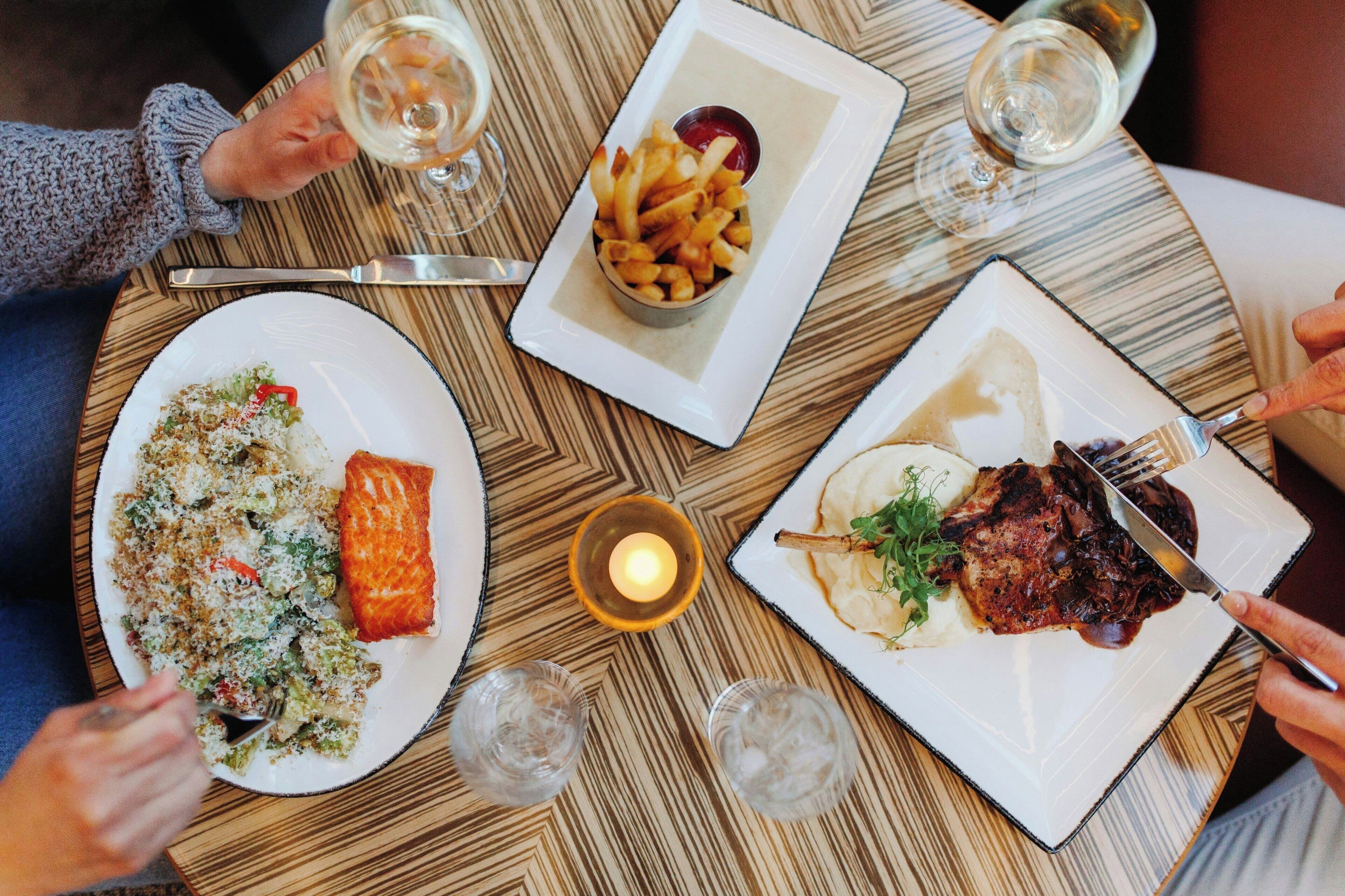 Una mesa redonda para comer con platos de comida, copas de vino y una vela encendida.