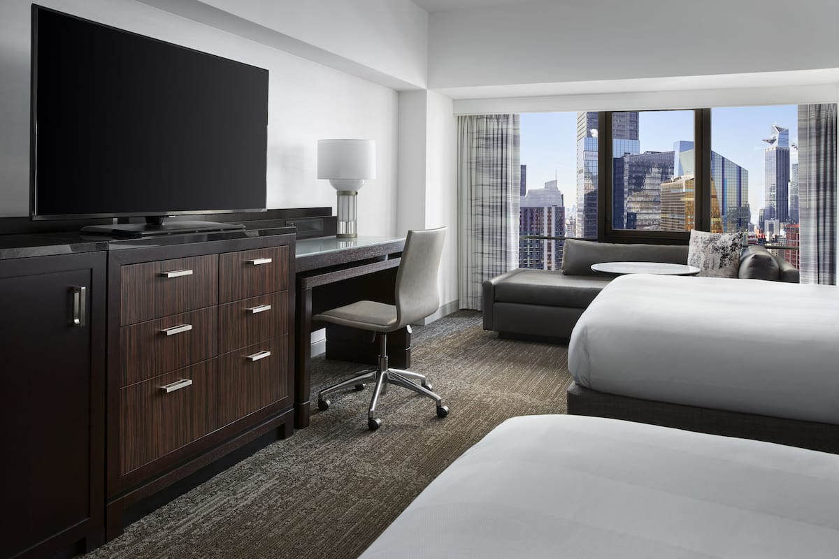 Een hotelkamer met een groot flatscreen televisietoestel, een bureau met stoel, een bank en een bed.