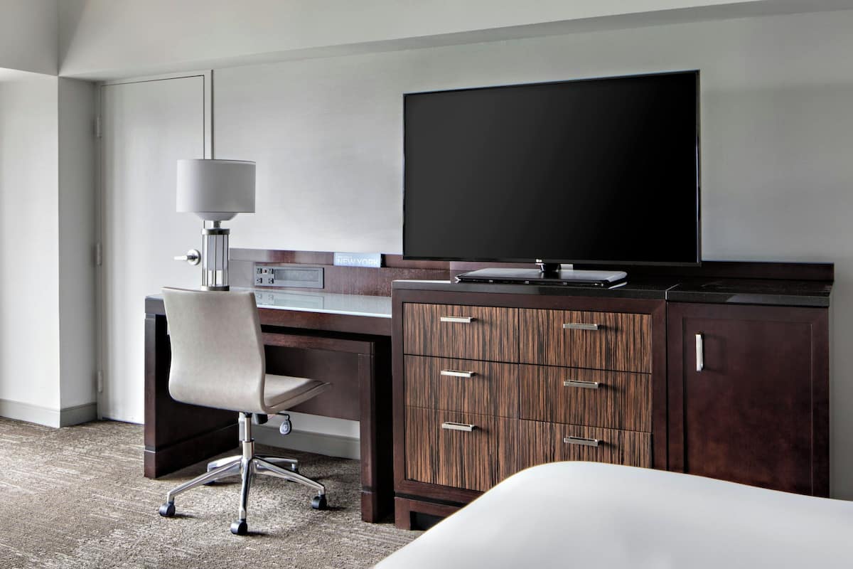 Een hotelkamer met een bureau, stoel, televisie en garderobe.