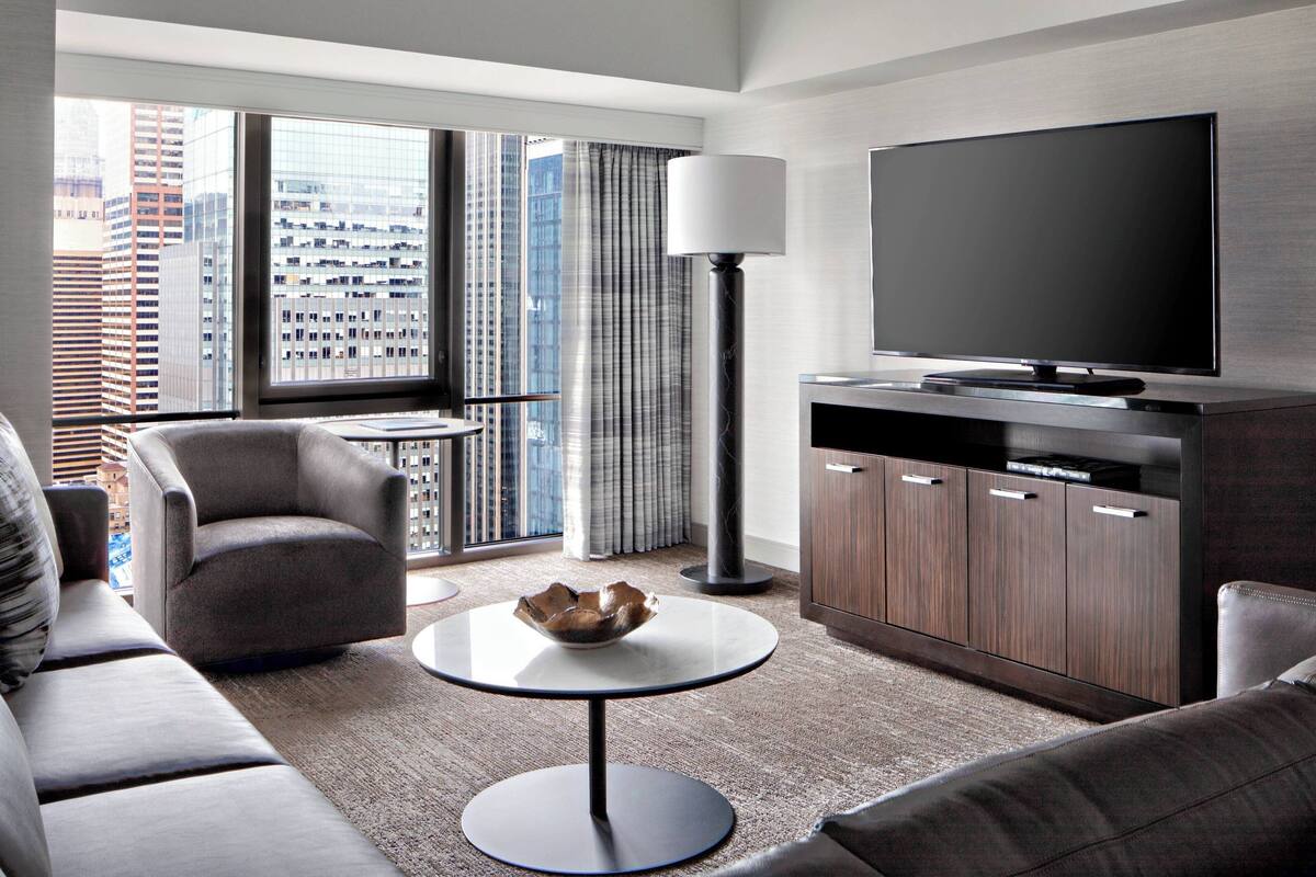Een moderne woonkamer met een bank, fauteuil, rond bijzettafeltje en een flatscreen televisie.