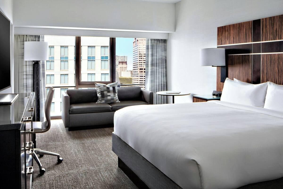 Een moderne hotelkamer met een groot bed, een slaapbank, een bureau en uitzicht op de stad.