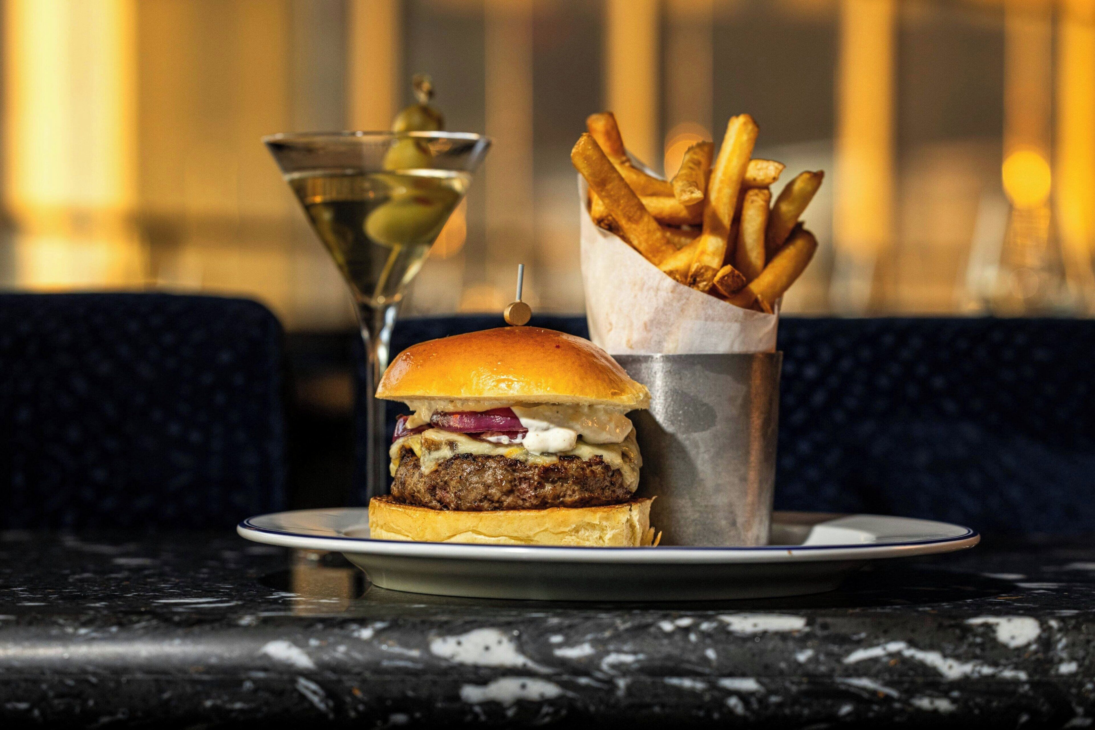 Una hamburguesa con papas fritas y un martini sobre una mesa.