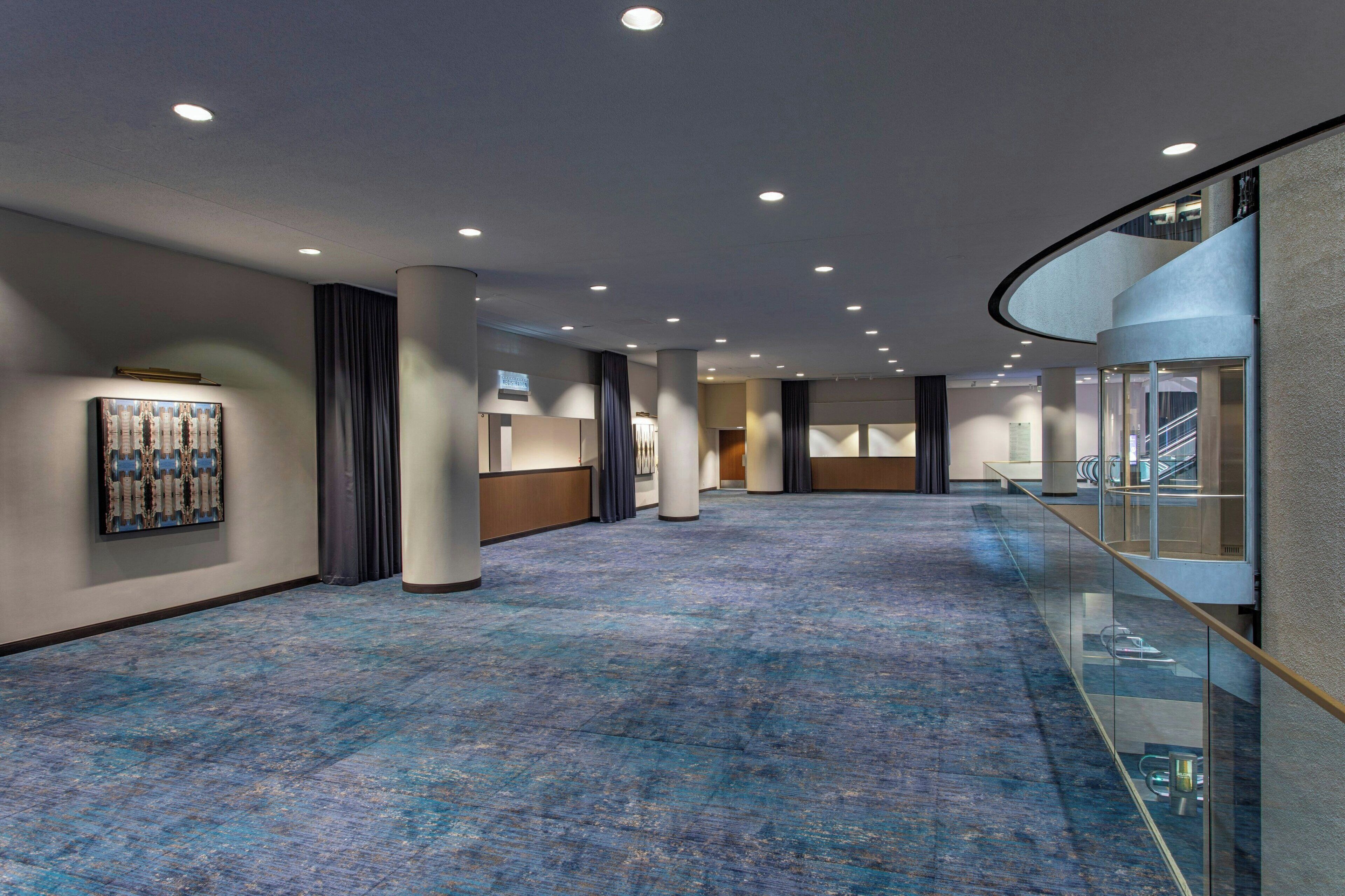 Un vaste couloir d’hôtel, doté d’une moquette bleue, d’une rambarde en verre et d’un design moderne au plafond.