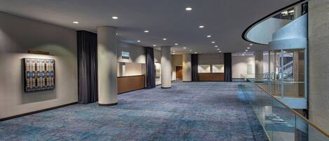 A spacious hotel corridor with a blue carpet, glass railing, and a modern ceiling design.