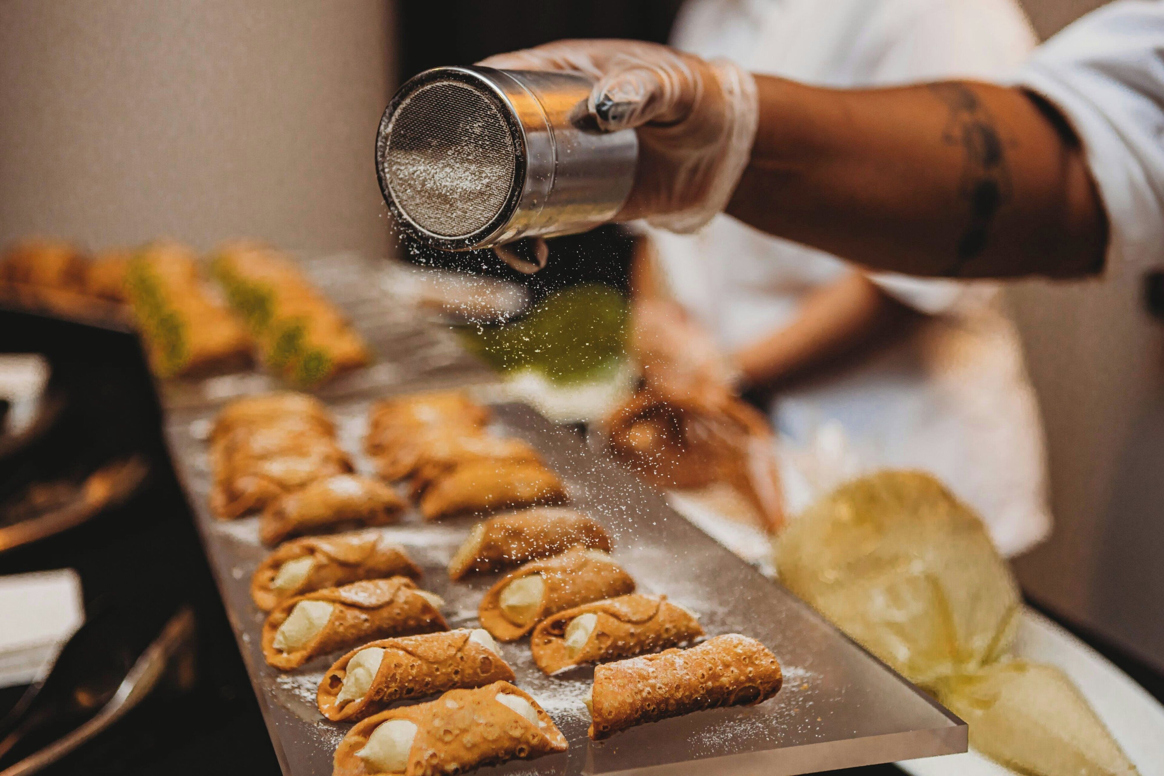 A person sprinkling powdered sugar over a tray of pastries.