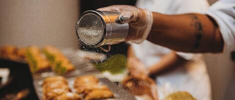 A person sprinkling powdered sugar over a tray of pastries.