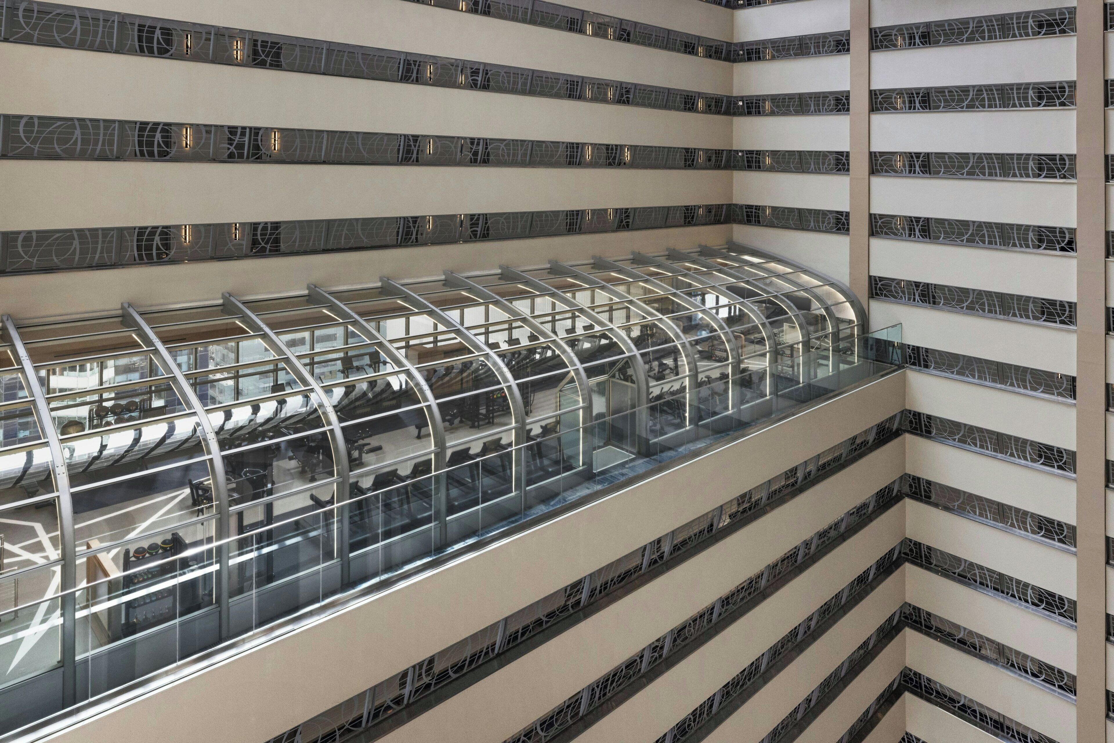 A multi-level interior with a glass-enclosed atrium, metallic railings, and patterned wall tiles.