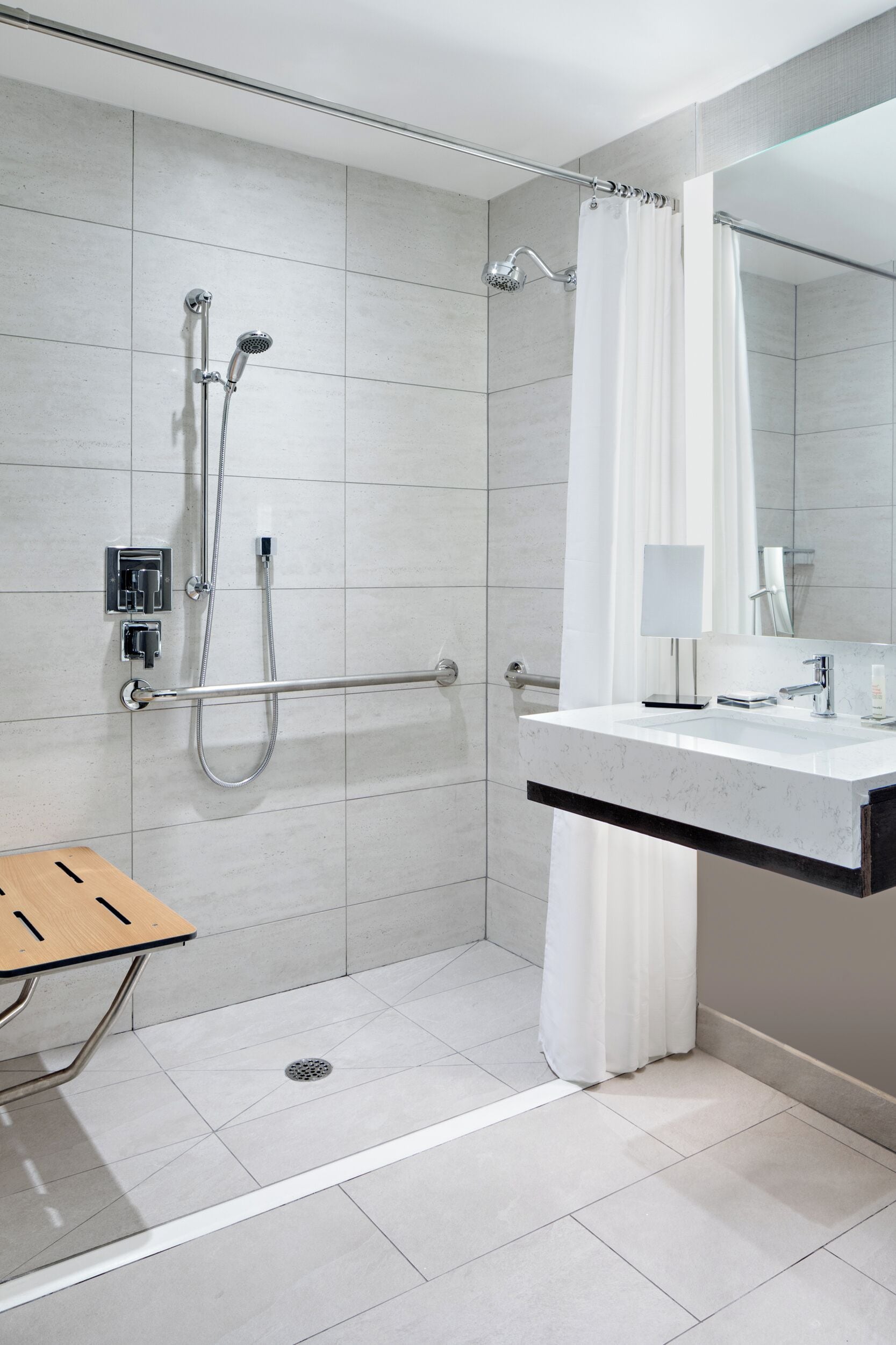 Un baño moderno con ducha, tocador con espejo y banco de madera.