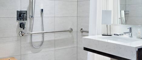Un baño moderno con ducha, tocador con espejo y banco de madera.