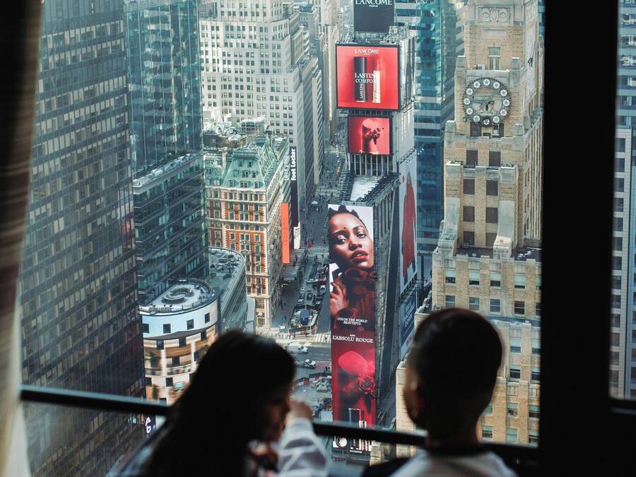 Une vue depuis une fenêtre donnant sur un paysage urbain, avec de hauts immeubles et des panneaux publicitaires.