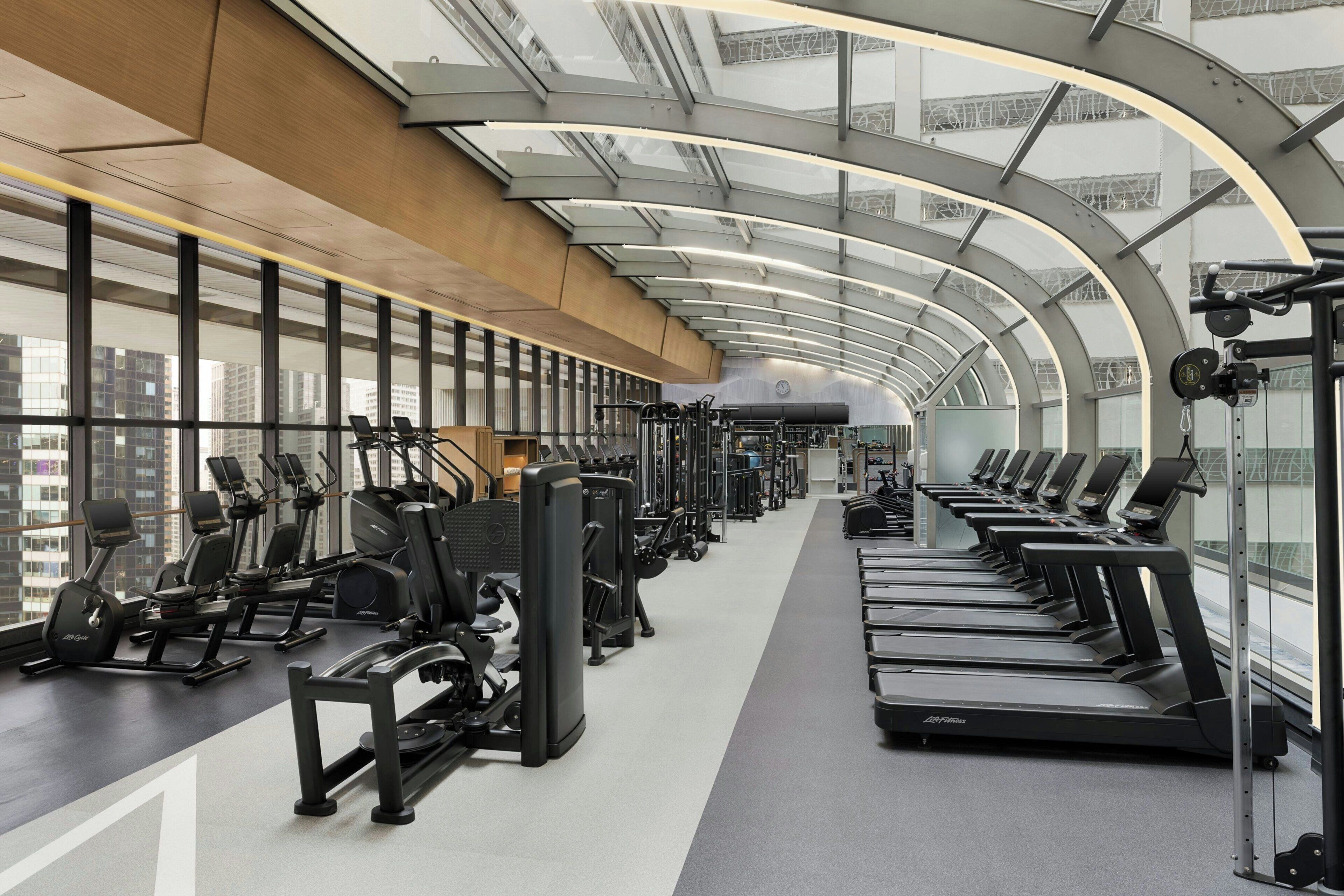 Un gimnasio con cintas de correr, elípticas y equipos de pesas, que cuenta con ventanas amplias y un techo curvo.
