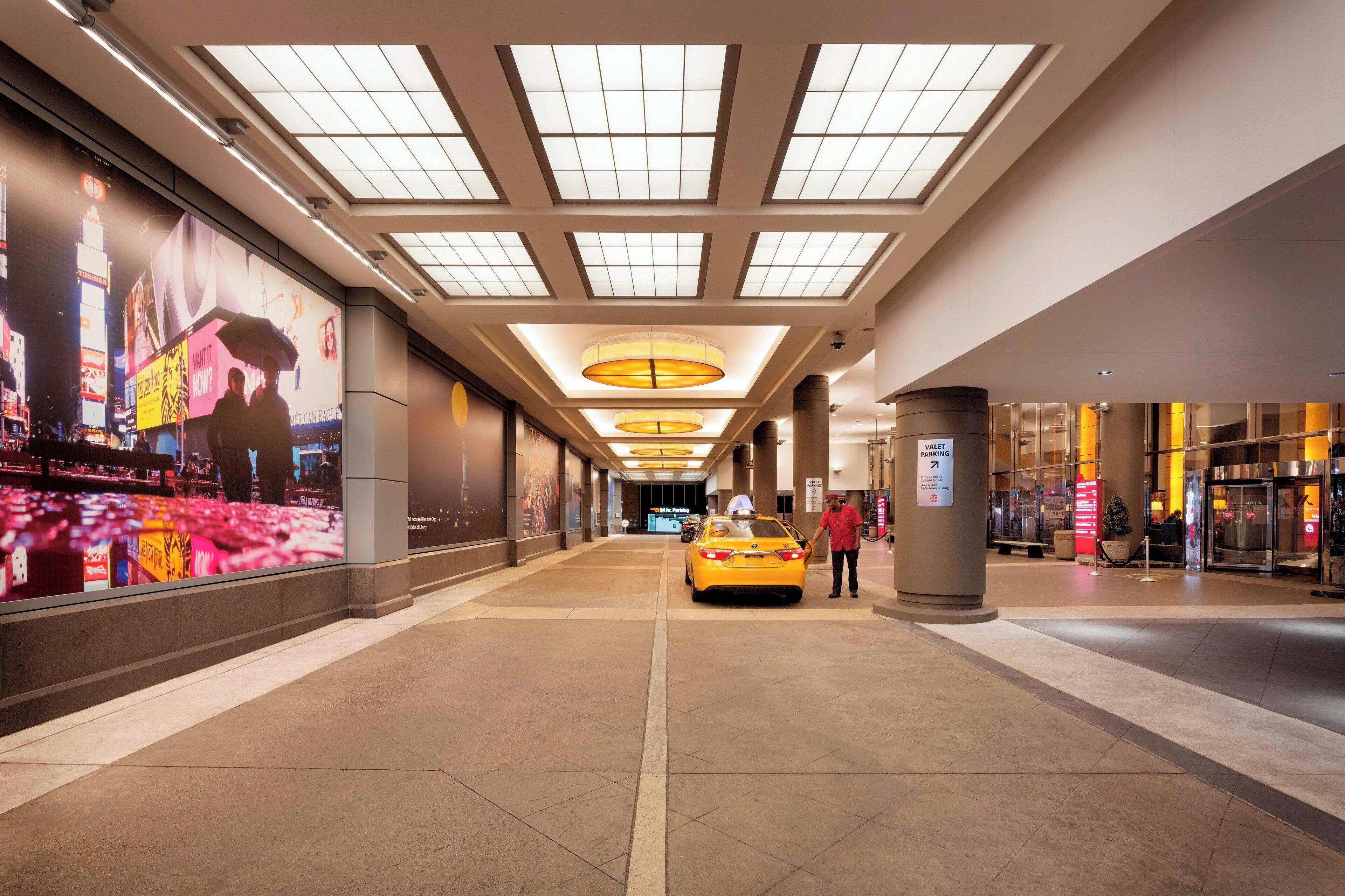 A corridor with a yellow taxi, a large advertisement on the left, and a pillar with a sign.
