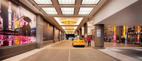 A corridor with a yellow taxi, a large advertisement on the left, and a pillar with a sign.