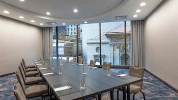A conference room with a long table, chairs, and large windows offering a view of a building with classical architecture.