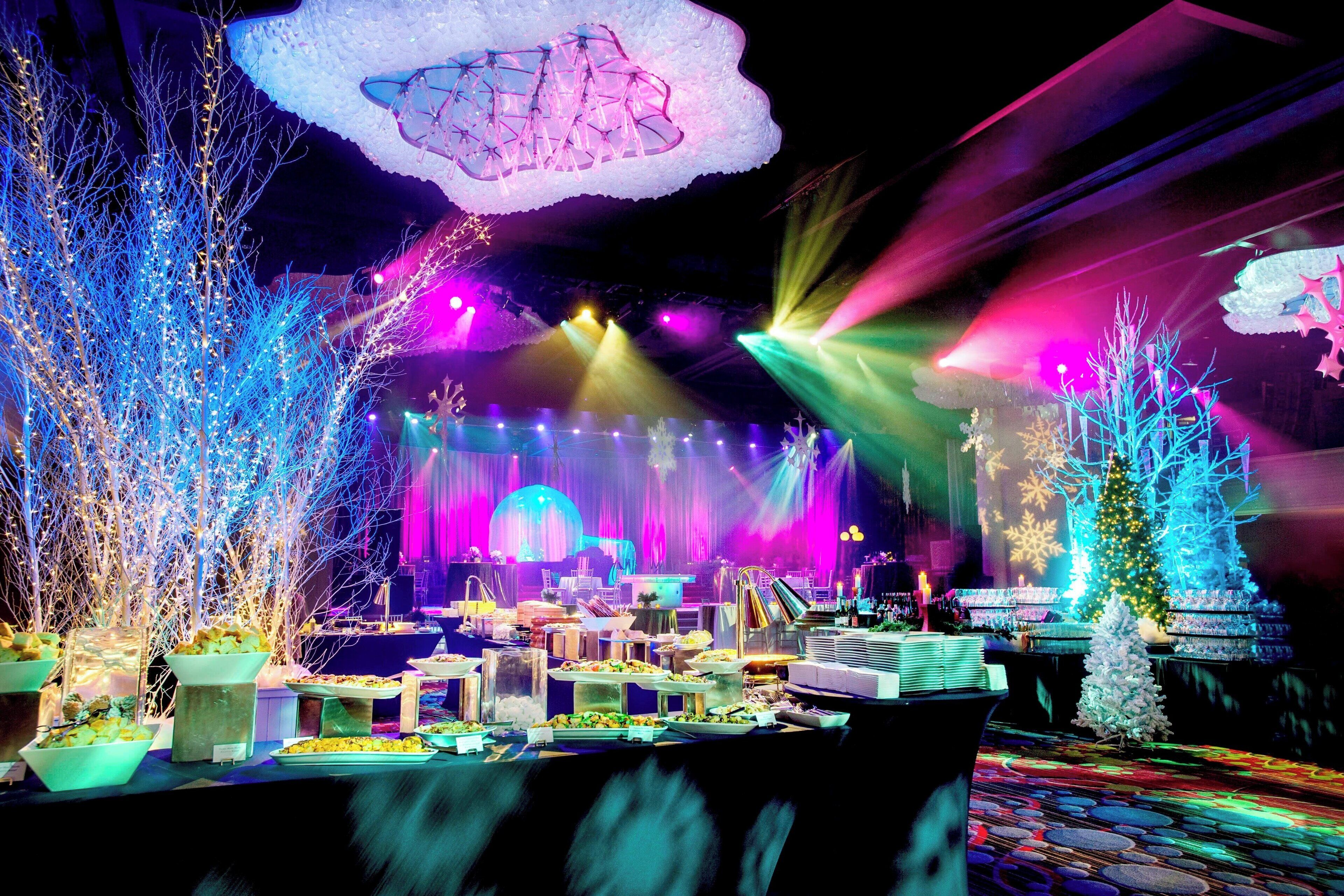 A festive indoor setting with a stage, illuminated trees, and a buffet table.