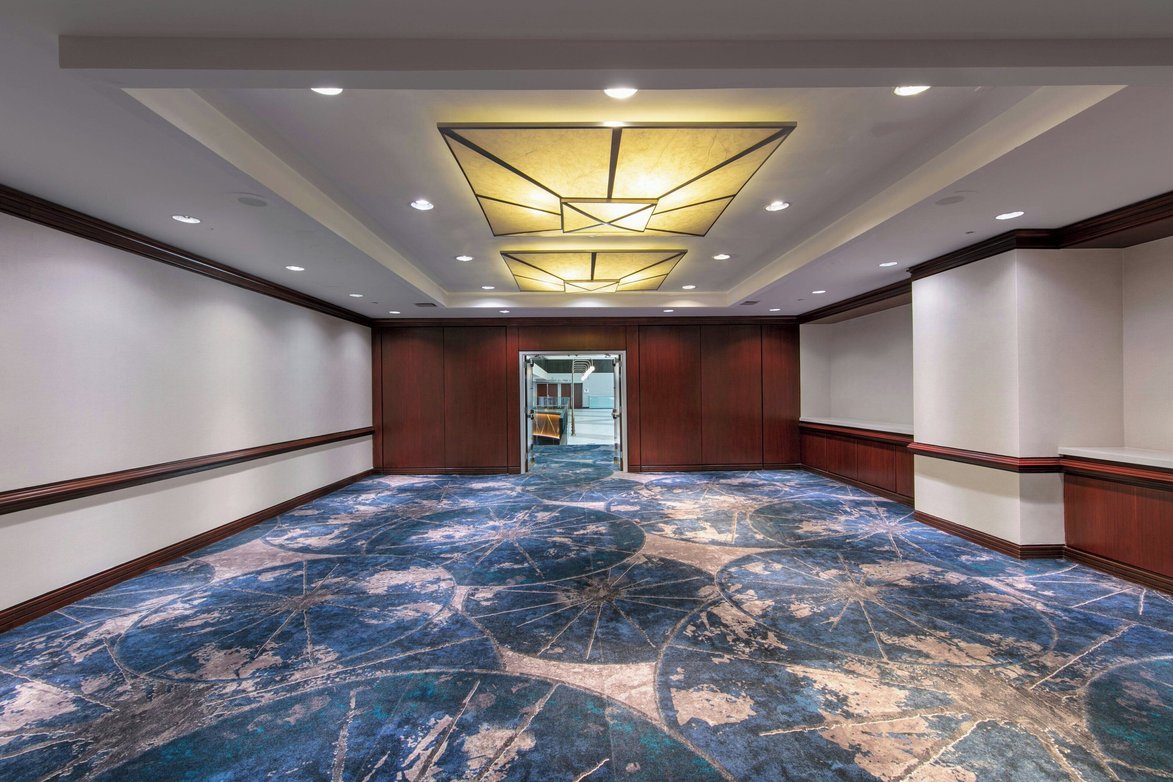 Un hall d’hôtel doté d’un tapis à motifs, de lambris en bois et d’un éclairage encastré.