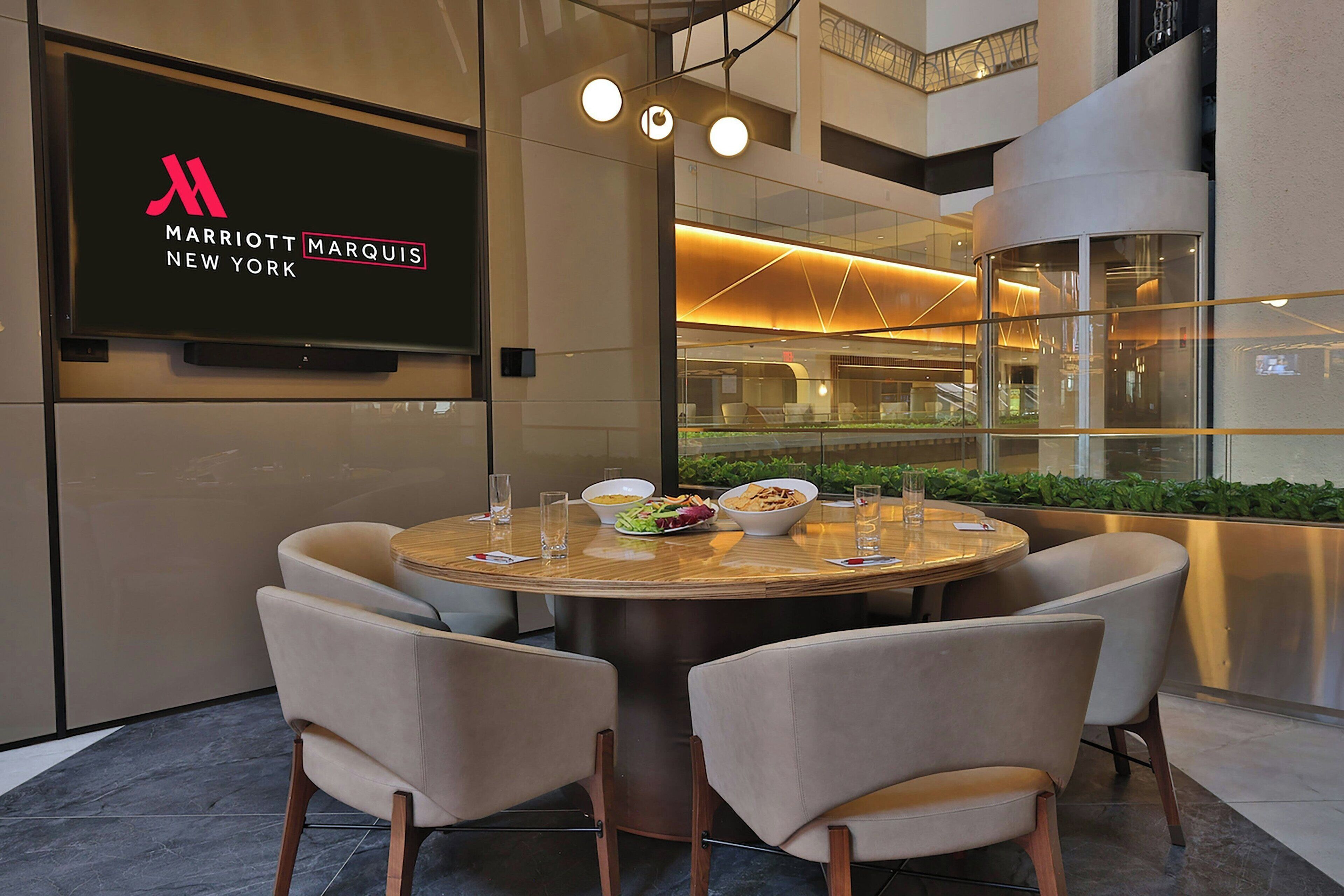 Un espace repas moderne avec une table ronde, six chaises et un grand écran affichant le logo du Marriott Marquis.