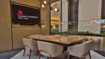Un comedor moderno con una mesa grande, cuatro sillas y un televisor mostrando el logotipo del Marriott Marquis New York.