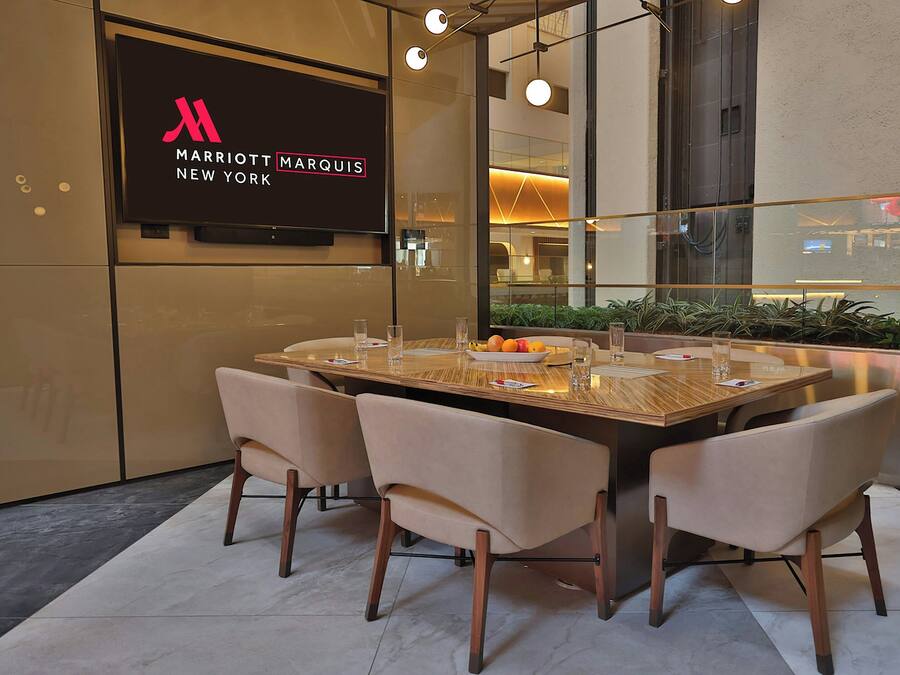 A modern dining area with a large table, four chairs, and a television displaying the Marriott Marquis New York logo.