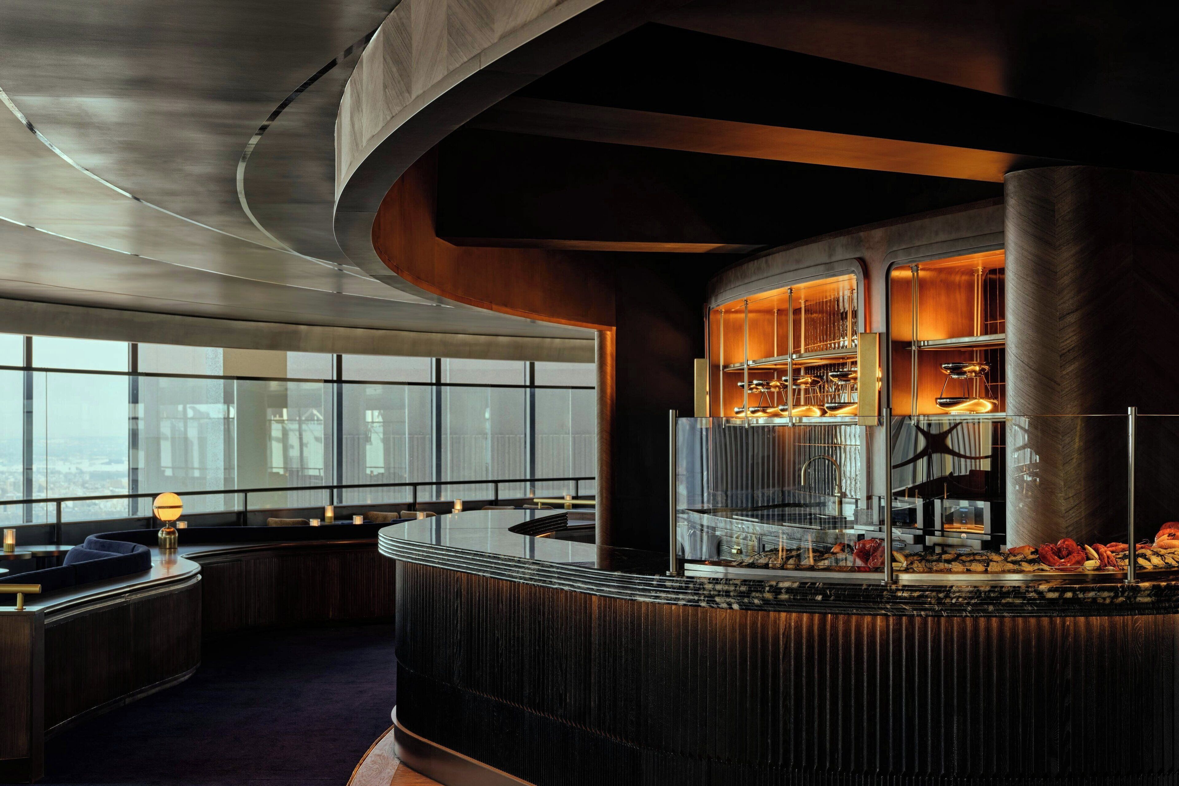 A modern bar area with a curved counter, seating, and a view of the city through large windows.