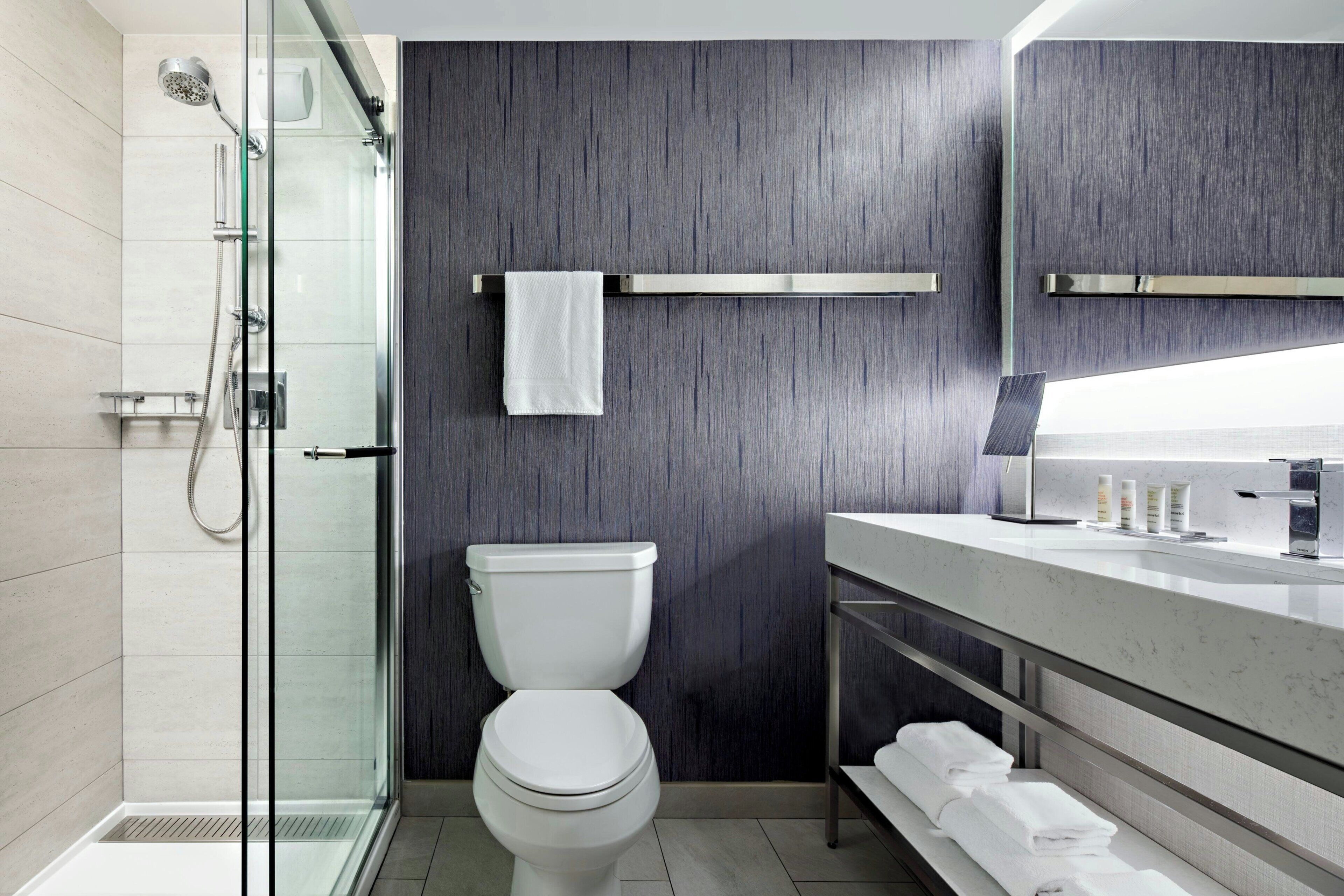 Un baño moderno con cabina de ducha de vidrio, inodoro blanco y tocador con espejo.
