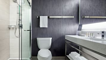 Un baño moderno con cabina de ducha de vidrio, inodoro blanco y tocador con espejo.