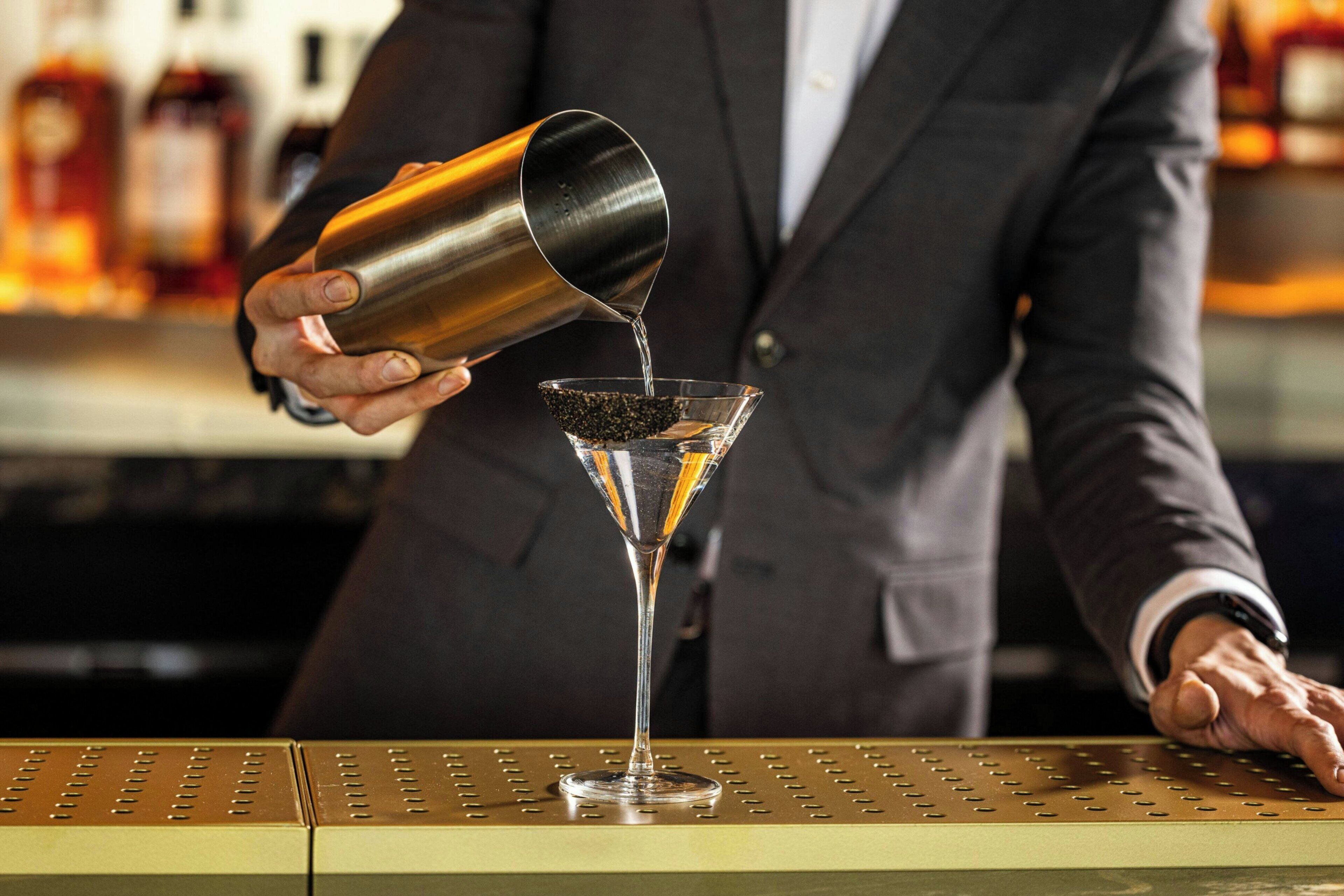 A person pouring a drink into a martini glass.