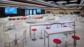 A modern hotel lobby with white furniture, red bar stools, and large screens displaying content.