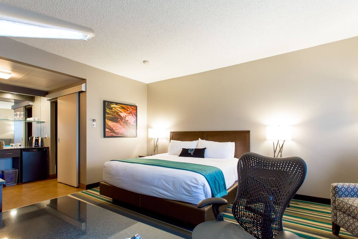 A hotel room with a bed, a chair, a desk with a computer, and a mirror.