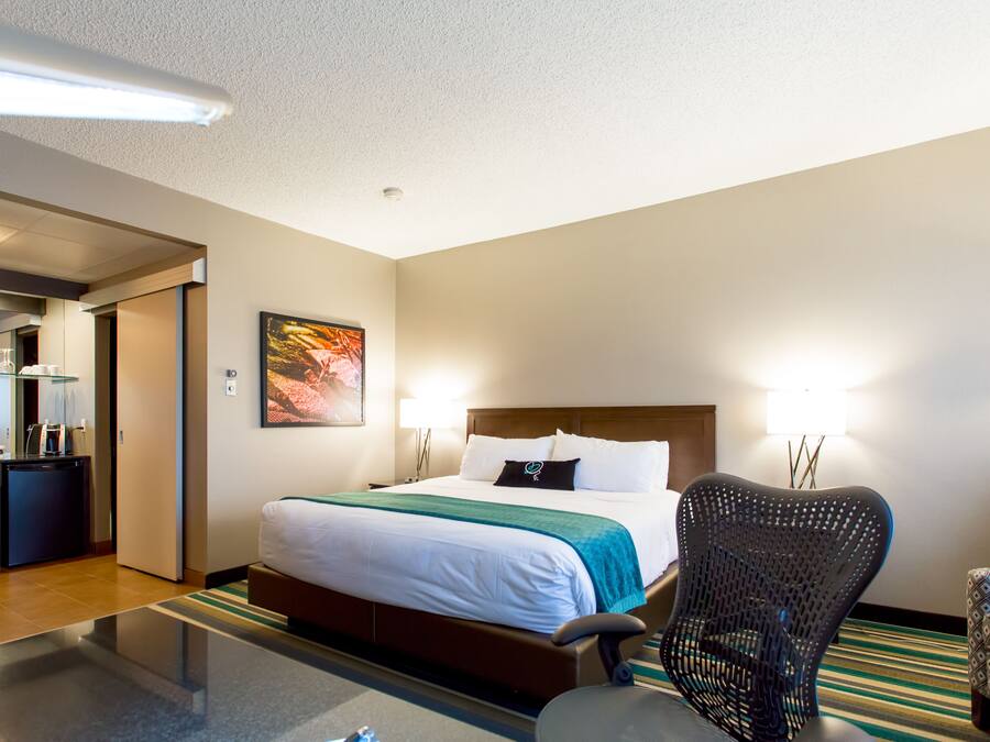 A hotel room with a bed, a chair, a desk with a computer, and a mirror.