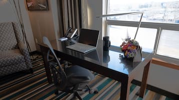 A hotel room with a desk, laptop, phone, mug, and a flower vase.