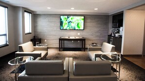 A modern room with a flat-screen TV mounted on the wall, a small table with a glass top, and two sofas. - Hotel Blackfoot (Calgary)