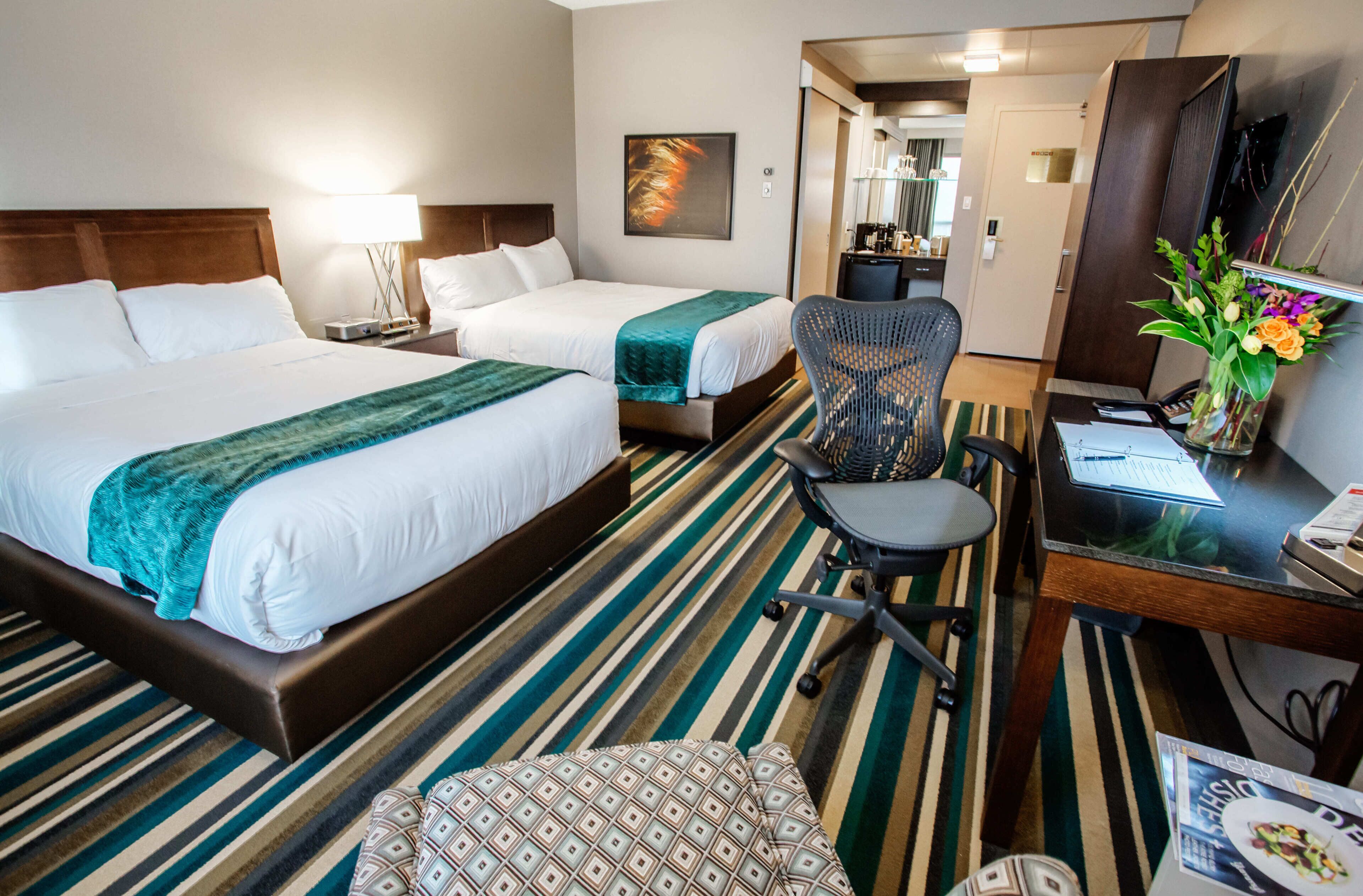 A hotel room with two beds, a desk, a chair, and a dining table.