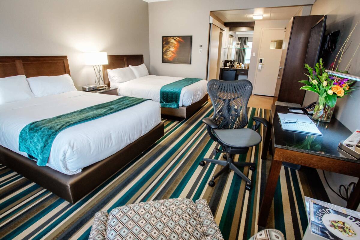 A hotel room with two beds, a desk, a chair, and a dining table.
