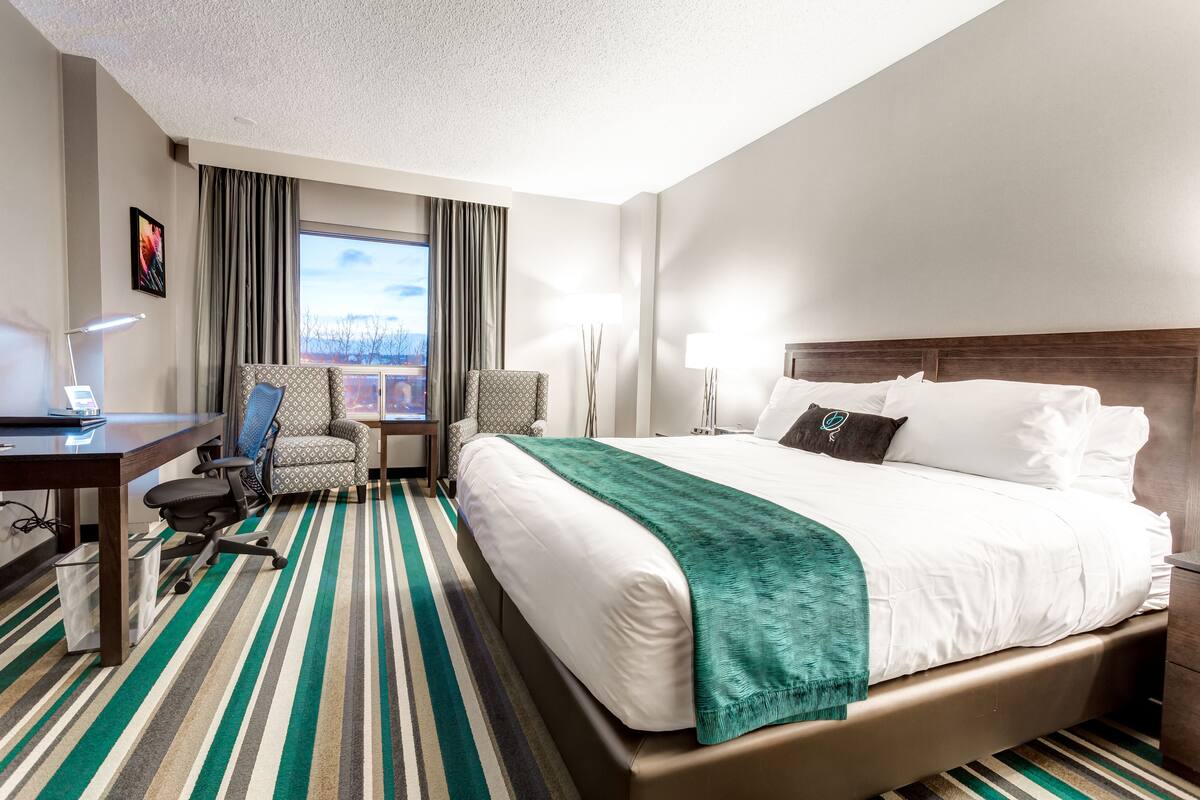 A hotel room with a large bed, a desk with a chair, a window with curtains, and a view of the cityscape.