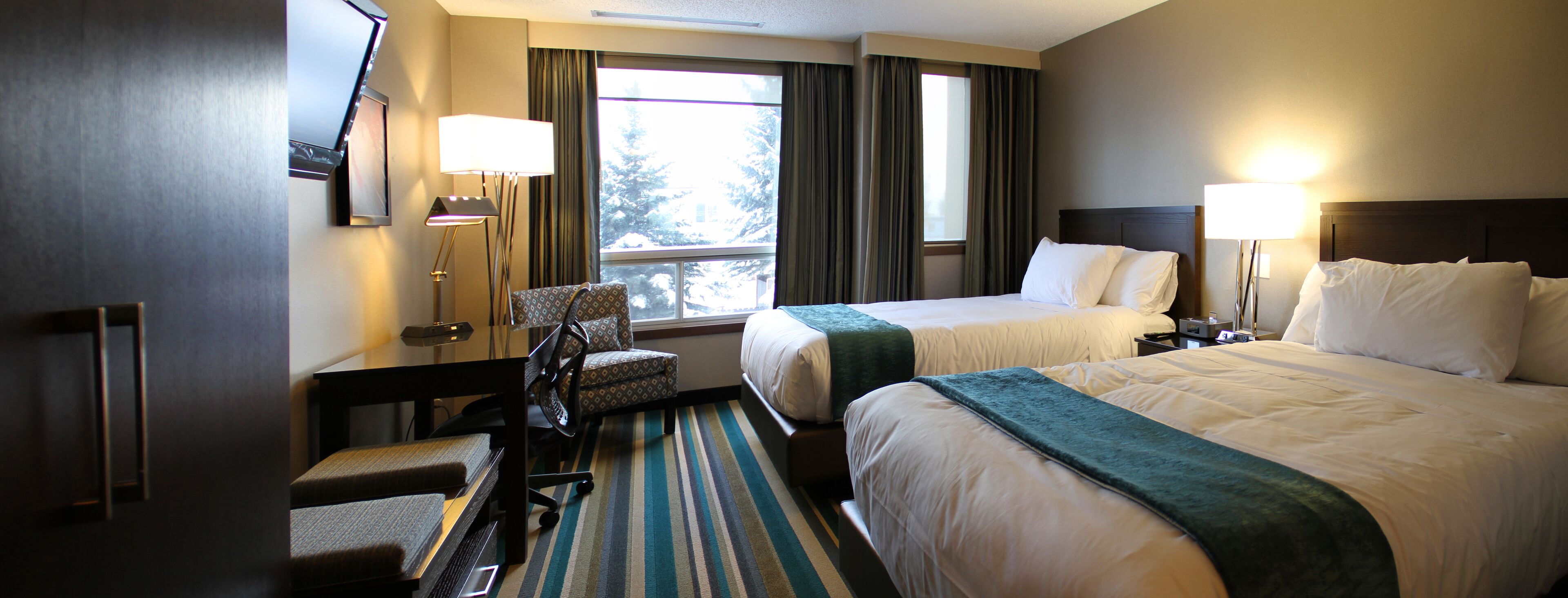 A hotel room with two beds, a desk, a chair, and a window with curtains.