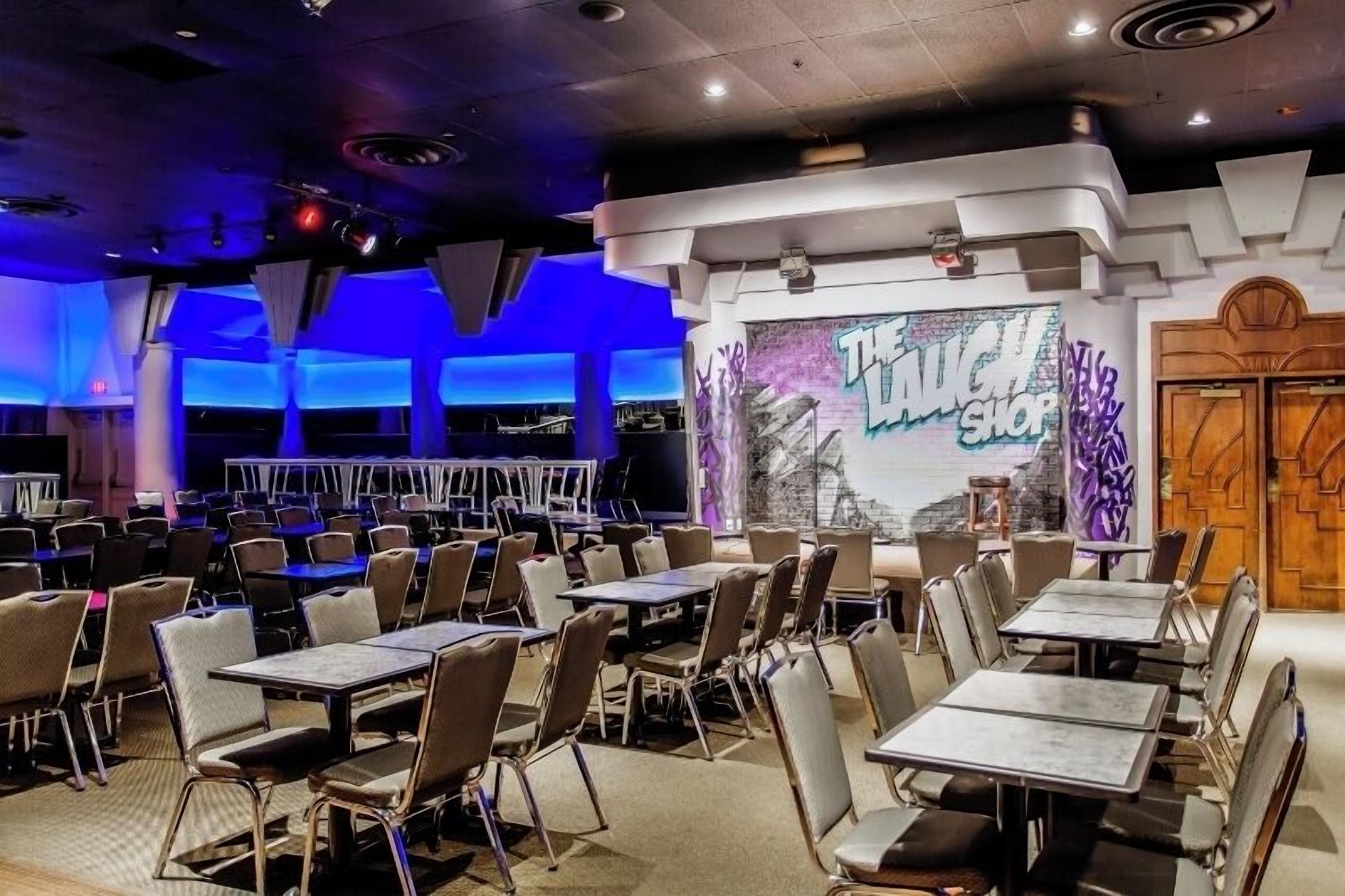 A conference room with tables and chairs, a stage with a backdrop, and a door with a wooden panel design.