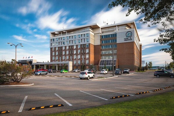 Een modern hotel met een opvallende ingang, meerdere parkeerplaatsen en een heldere lucht.