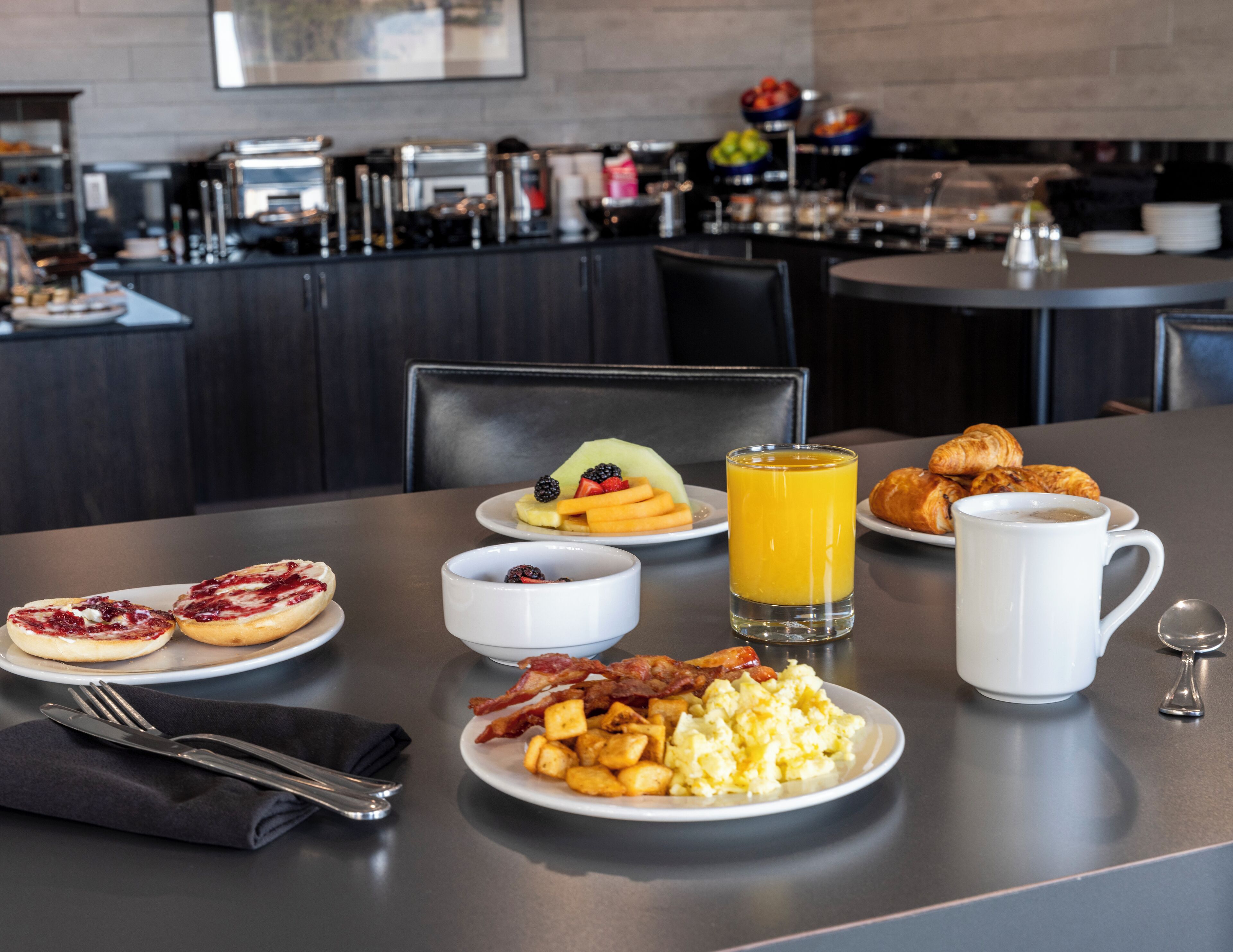 A breakfast setting with plates of eggs, bacon, toast, fruit, and juice.