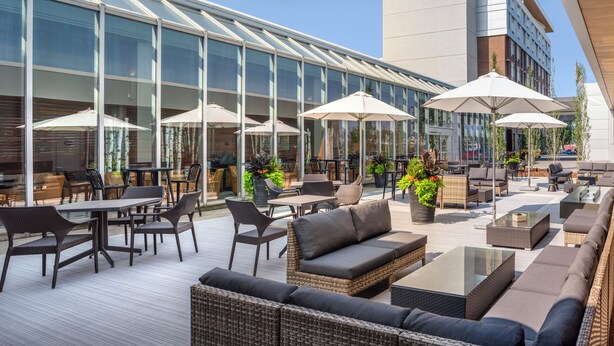 An outdoor seating area with wicker furniture, white umbrellas, and potted plants. - Hotel Blackfoot (Calgary)