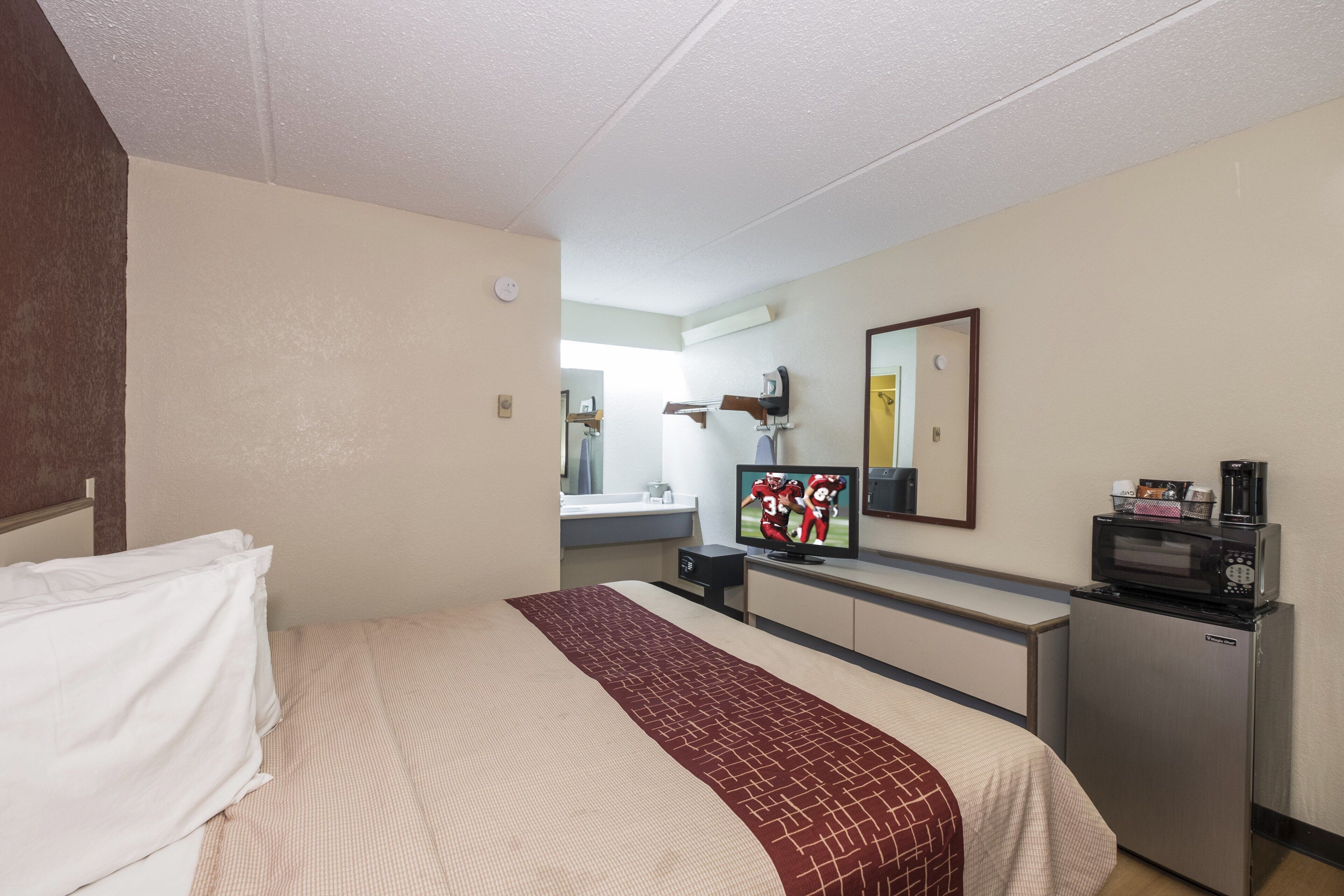 A hotel room with a bed, a desk with a computer, a microwave, and a small refrigerator.