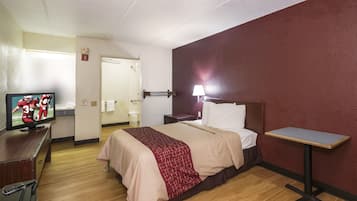 A hotel room with a bed, bedside table, lamp, TV, and a wooden dresser.