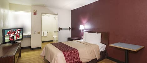 Ein Hotelzimmer mit einem Bett, Nachttisch, Lampe, Fernseher und einem Holzschrank.